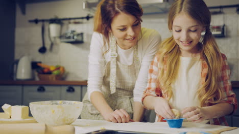 Smiled-pretty-mother-and-daughter-in-aprons-putting-daugh-in-the-forms-for-baking-muffins-in-the-cozy-kitchen.-Indoor